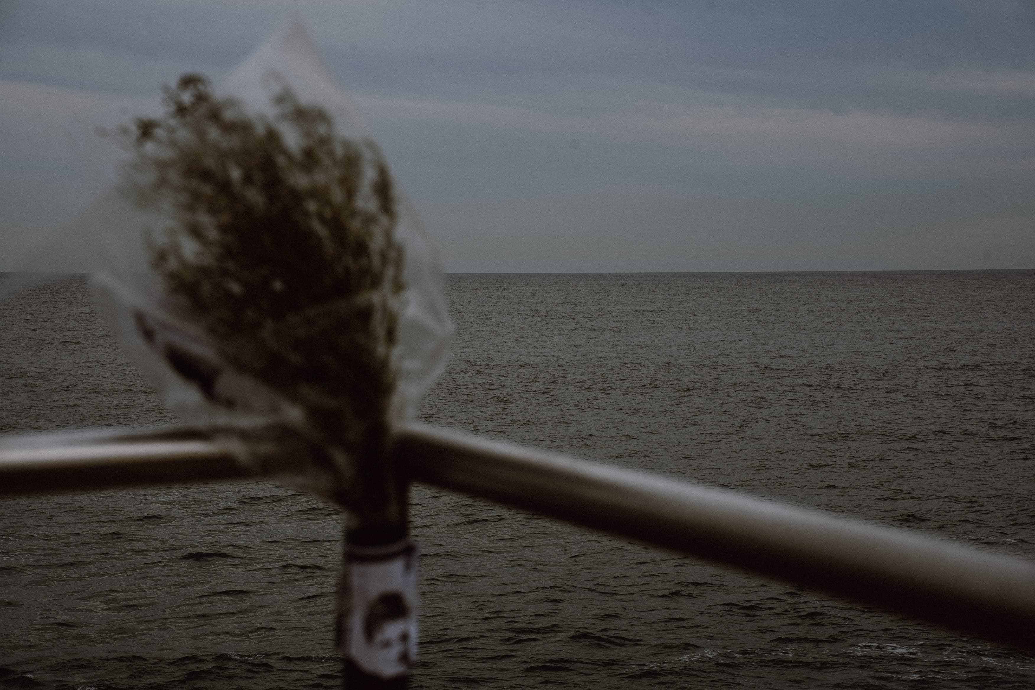 Flowers wrapped in plastic wedged into a boat railing over the ocean