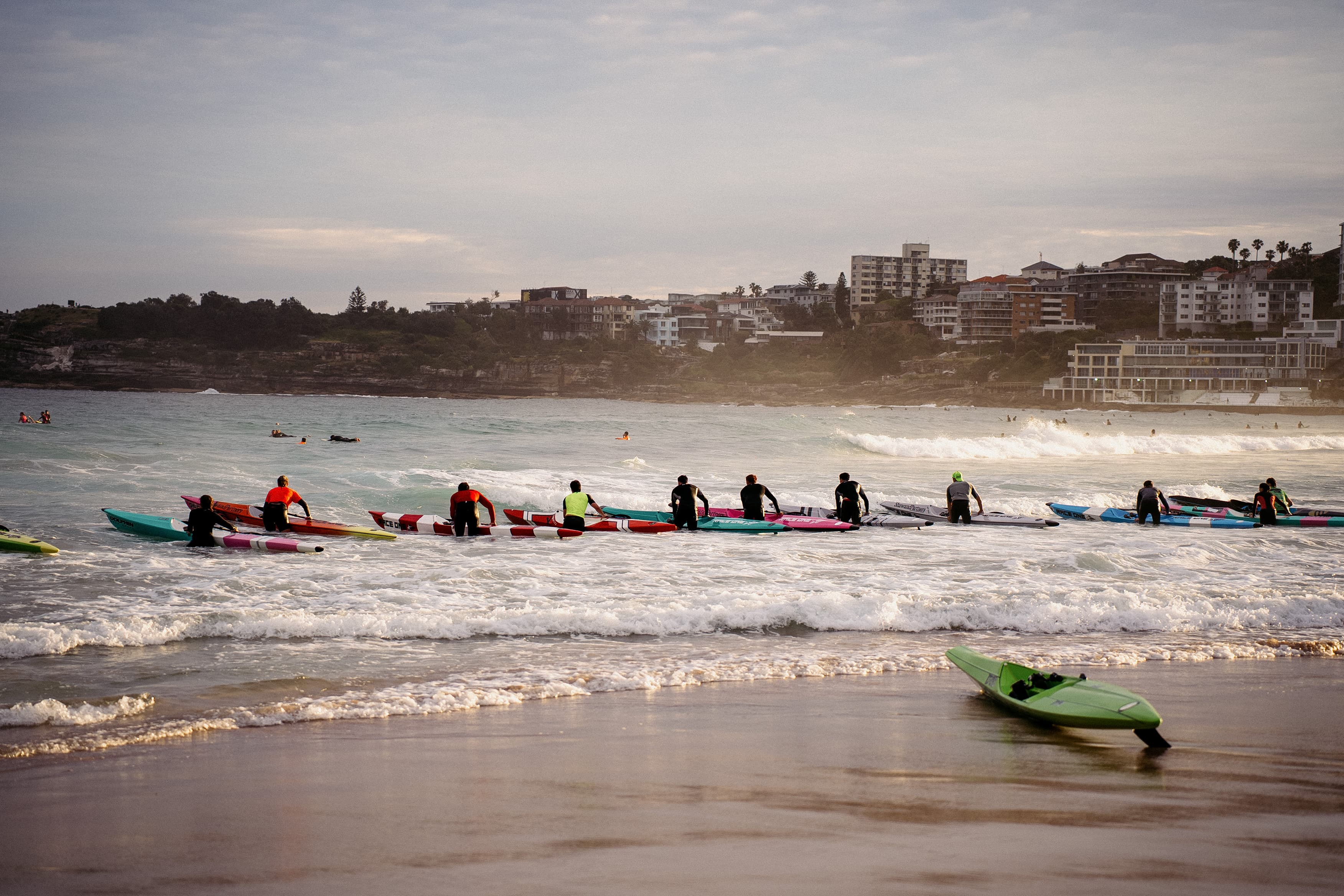 A line of surf-ski paddlers pushing out through the break in the evening