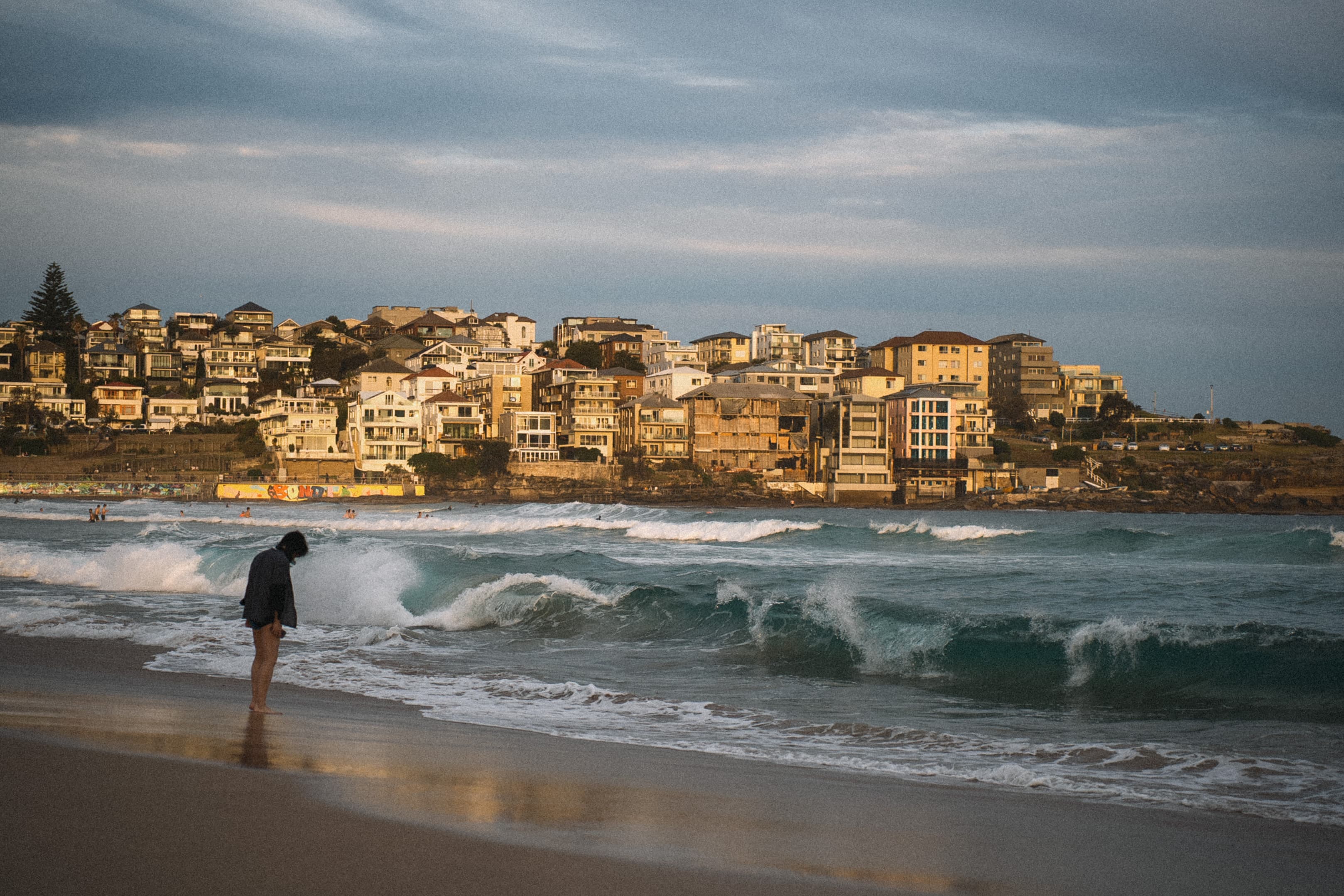 A lone figure standing at the water's edge as waves roll in