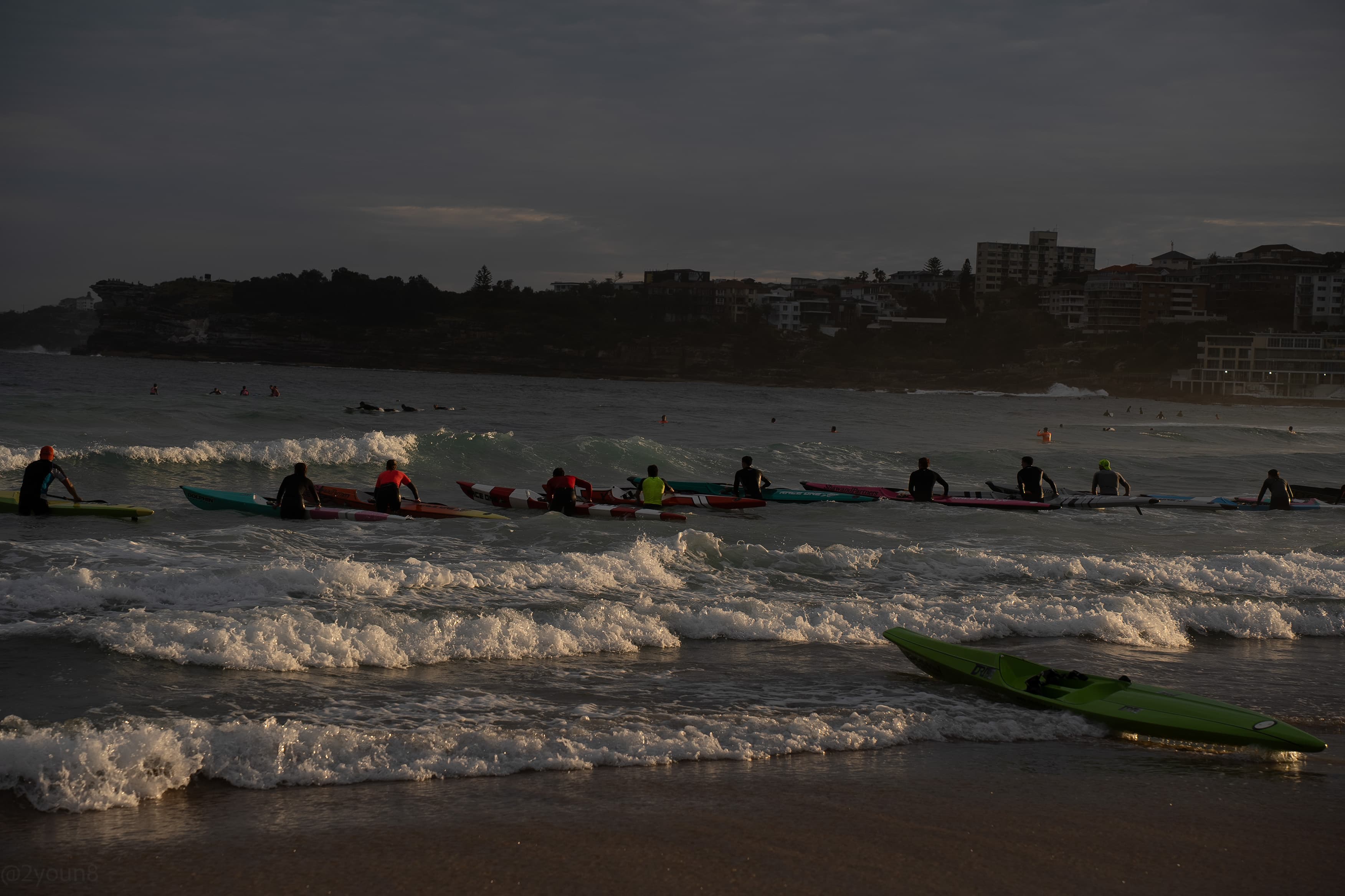 Paddlers crossing the break as the headland fades into dusk haze