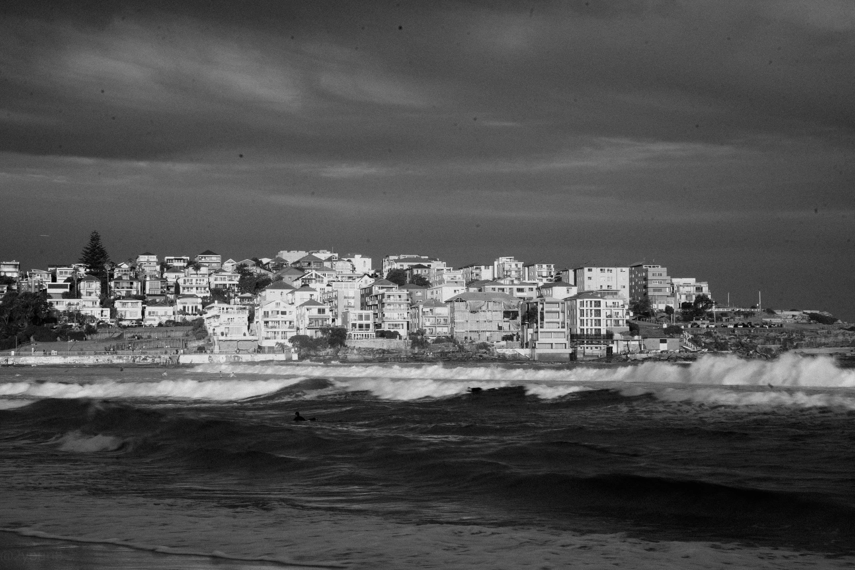 Black and white photo of the surf below cliffside apartments